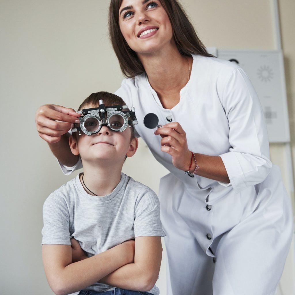 Doctor tuning the phoropter to to determine visual acuity of the little boy