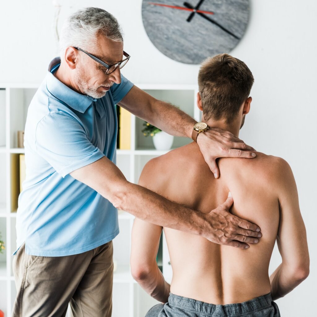 bearded doctor in glasses touching back of shirtless patient in clinic